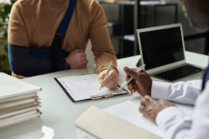man in a sling signing paperwork