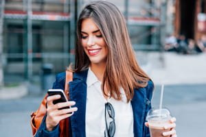 woman holding a coffee while looking at a cellphone