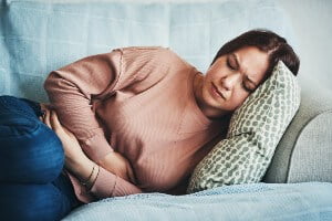 young woman lying on sofa with stomach pain