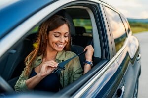 young woman in driver's seat fastening seat belt
