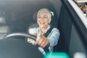 mature woman wearing headphones and drinking coffee while driving