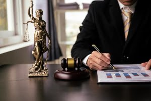 Someone writing on a paper with a gavel placed on the table.