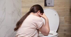Women by a toilet feeling nauseous.