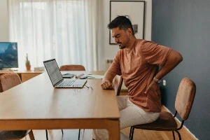 A person with back pain in front of a laptop.