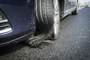 A blue car with a tire blowout on the front wheels on the road.