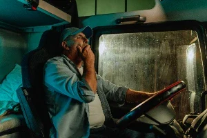 A truck driver at night yawning while behind the wheel
