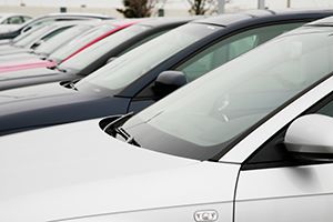 Row of parked cars in various colors closely lined up in an outdoor lot, focusing on side mirrors and windshields.